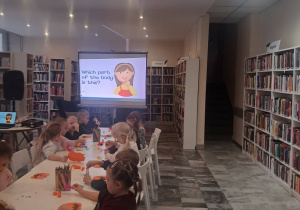 Dzieci siedzą przy stoliku i wykonują pracę plastyczną-dynię.