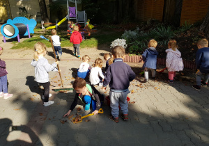 Najmłodsze dzieci sprzątają liście w ogrodzie.