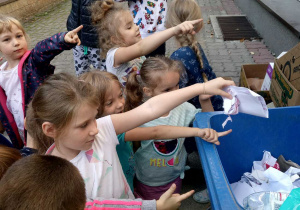 Dzieci wyrzucają papiery do niebieskiego kosza.