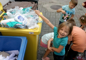Dziewczynka wyrzuca plastik do żółtego kosza.