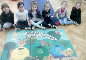Dziewczynki z grupy Pandy przed ułożonymi puzzlami. Hasło na puzzlach brzmi - Bądź ekobohaterem - segreguj odpady.