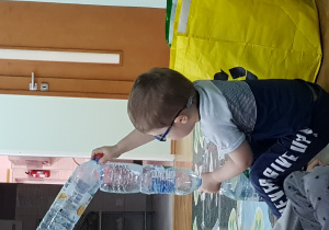 Chłopiec buduje z pustych butelek PET.