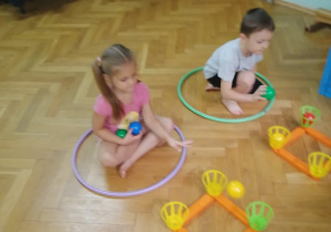 Dzieci wrzucają piłeczki do kubeczków umieszczonych w wierzchołkach kwadratów - gra Serso Mej.