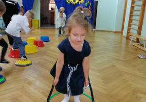 Dziewczynka przeskakuje obunóż przez kołową drabinkę.