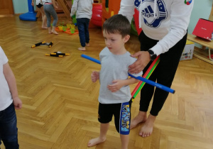 Pan Witek tłumaczy dzieciom ćwiczenie z drążkiem gimnastycznym na przykładzie chłopca.