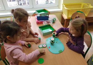 Dziewczynki układają wieżę dla plastikowych żabek.