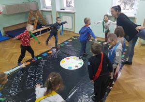 Dzieci stoją na jednej nodze podczas gry w "Kolorowe kształty przedszkolaka".