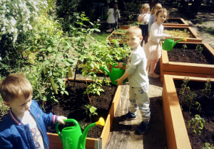 Dzieci z konewkami przy skrzyniach ogrodowych.