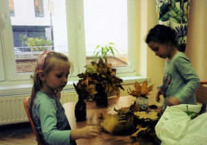Dziewczynki układają kompozycje z liści do wazonu, by ozdabiały salę