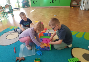 Troje dzieci buduje wspólnie zagrodę.