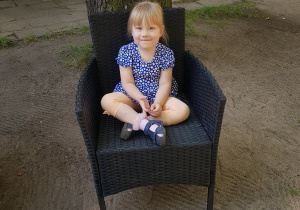 Dziewczynka siedzi na fotelu ratanowym w ogrodzie.