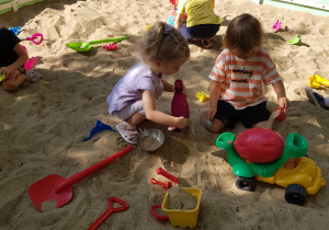 Kilkoro maluszków bawi się w piaskownicy.