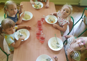 Sześcioro dzieci siedzi przy stole i je zupę.