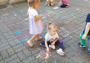 Dzieci rysują kredami na betonowych kostkach.