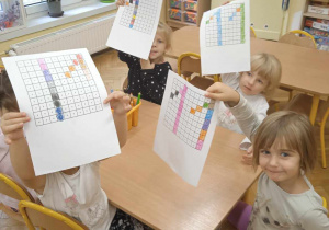 Dziewczynki siedzą przy stoliku i pokazuje prace ilustrujące kod binarny