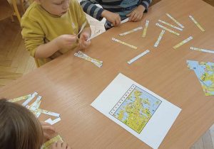 Dzieci siedzące przy stoliku układają obrazek z pociętych kawałków