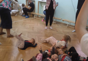 Dzieci leżą na podłodze pod ruszaną przez rodziców chustą animacyjną.