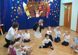 Dzieci siedzą w kolena podłodze i pokazują jedno ucho.