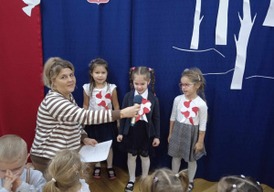 Ola, Martynka i Oliwka z grupy Małpek prezentują swoje wiersze. Pani Małgosia trzyma mikrofon dzieciom.
