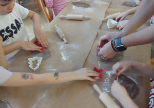 Dzieci wykrawają foremkami różne kształty ciasteczek.