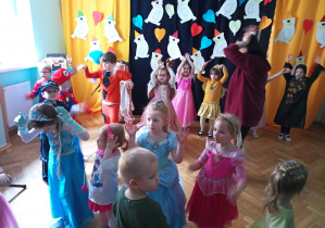 Dzieci w kolorowych strojach tańczą i naśladują ruchy prowadzącej.
