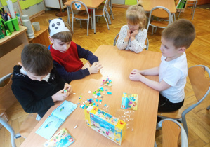 Chłopcy budują według instrukcji zestaw z klocków Lego a dziewczynka przygląda się im.