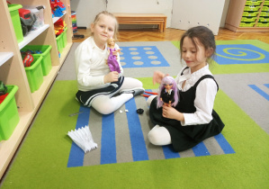 Dwie dziewczynki siedzą na dywanie i bawią się zabawkami.