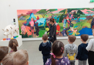 Przewodniczka angażuje dzieci do opisywania kolorów obrazu panoramicznego przy wejściu do galerii.