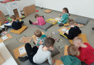 Grupa dzieci siedzących na wygodnych poduchach tworzy portret Nietoperza Emilki.