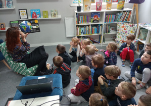 Dzieci oglądają książkę o układzie słonecznym, którą pokazuje pani bibliotekarka.