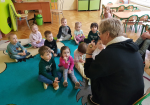 Pani Dyrektor tłumaczy dziecio co znaczy swięto grupy, dziecisiedzą przed nią na dywanie.