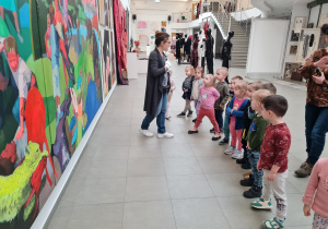 Dzieci stoją przed dużym obrazem, oglądają go i nazywają użyte przez autora kolory.