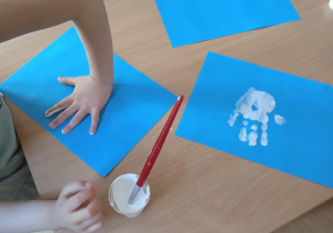 Dziecko odbija rączkę pomalowaną białą farbą na kartce papieru