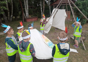 Chłopcy z "Żyrafek" budują tipi nakładając materiał na konstrukcję z długich gałezi.