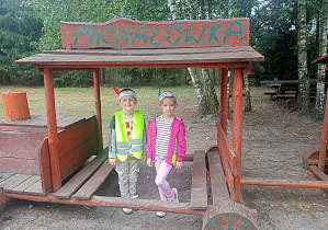 Chłopiec z dziewczynką z Żyrafek pozują do pamiątkowego zdjęcia pod drewnianym daszkiem.
