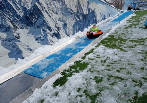 Dziewczynka zjeżdża z wysokiej zjeżdżalni na oponie.