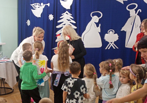 Pod opieką wychowawczyni delegacja przedszkolaków z najstarszej grupy dziękuje za spotkanie: dzieci wręczają kwiaty i rysunki.