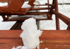 Bałwanek ze śniegu stoi na drewnianej ławce.