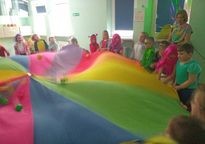 Dzieci turlają małe kolorowe piłeczki po chuście.