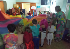 Pani Bergamutka tłumaczy dzieciom kolejną zabawę z wykorzystaniem chusty.