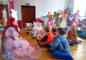 Przedszkolaki siedzą zasłuchane w pieśń przewodniczki.