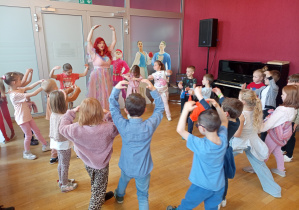 Dzieci unoszą jedną rękę nad głowę.