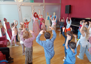 Dzieci naśladują ruchy i podnoszą obie ręce do góry.