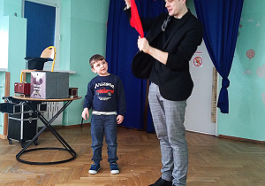 Chłopczyk przygląda się jak magik wyciąga czerwoną chusteczkę z drugiej dłoni.