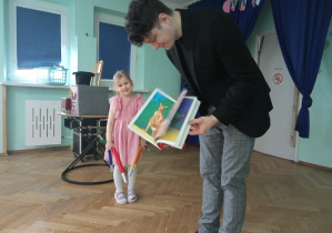 Dziewczynka ogląda książeczkę z niedowierzaniem.