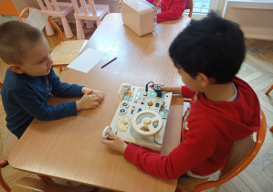 Chłopcy przy stoliku oglądają symulator samochodowy.