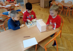 Trzech chłopców przy stoliku ogląda nowe zabawki.