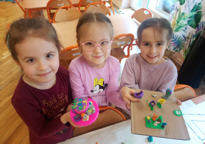 Trzy dziewczynki prezentują swoje dzieła z plasteliny.