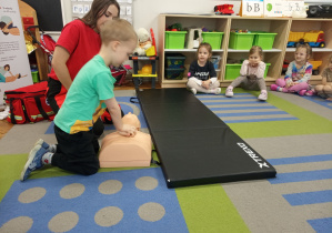 Chłopczyk wykonuje uciśnięcia klatki piersiowej na fantomie.