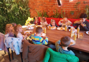 Przedszkolaki czekają przy stołach na pizzę.